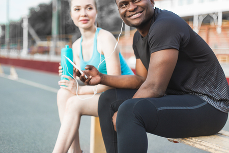Group of athletes sitting on the bench and resting after hard street workout session. Man and woman doing urban sport. rest after sports, listen to music, drink waterの写真素材