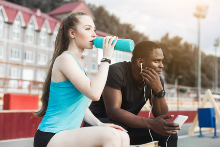Group of athletes sitting on the bench and resting after hard street workout session. Man and woman doing urban sport. rest after sports, listen to music, drink waterの写真素材