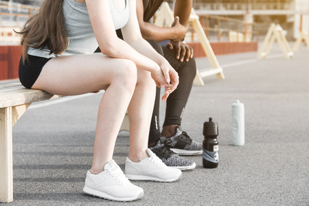 Group of athletes sitting on the bench and resting after hard street workout session. Man and woman doing urban sport. rest after sports, listen to music, drink waterの写真素材
