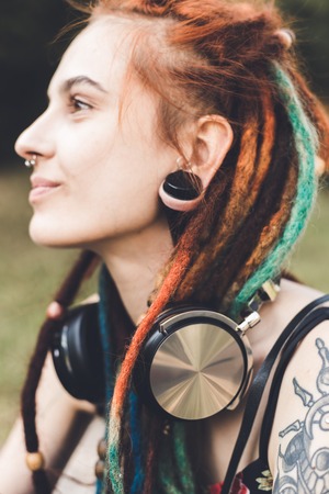 young girl with tattoo and dreadlocks listening to music in the parkの写真素材