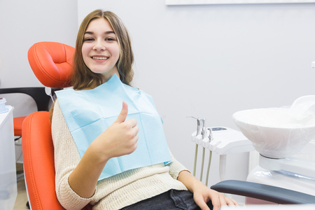 Dental clinic. Reception, examination of the patient. Teeth care. Young girl shows thumb up sign in dentist officeの写真素材