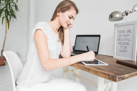 Young business woman working at home and draws on the tablet. Creative Scandinavian style workspaceの写真素材