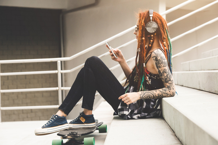 young girl with tattoo and dreadlocks listening to music while sitting on the stepsの写真素材