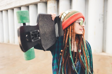 young girl in sun glasses and a cap stands with a longboard against the background of concrete structureの写真素材