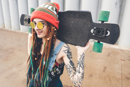 young girl in sun glasses and a cap stands with a longboard against the background of concrete structureの写真素材