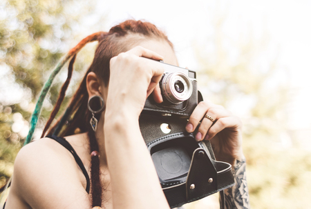 young girl with tattoos and dreadlocks photographs vintage camera in the parkの写真素材