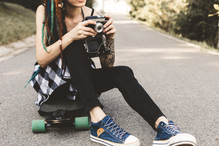 young girl with tattoos and dreadlocks photographs vintage camera in the parkの写真素材