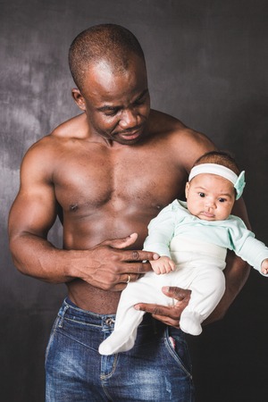 Muscular African American man holding a child against a black wallの写真素材