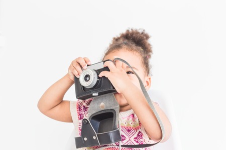 Portrait of a little girl in a colorful dress taking pictures on an old vintage camera