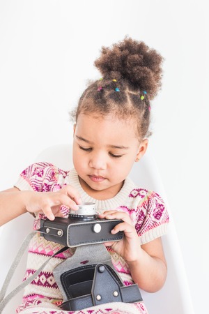 Portrait of a little girl in a colorful dress taking pictures on an old vintage cameraの写真素材