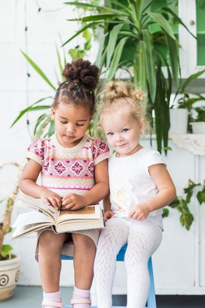 Two little girls read a book on the background of plants in potsの写真素材