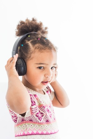 Cute little girl in a colorful dress listening to music with headphones on a white backgroundの写真素材