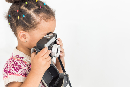 Portrait of a little girl in a colorful dress taking pictures on an old vintage cameraの写真素材