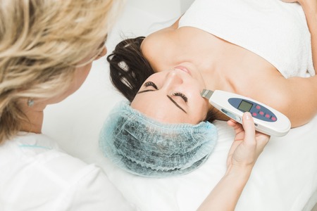 Beautician does the procedure of ultrasonic face cleaning for a young woman in a beauty salon