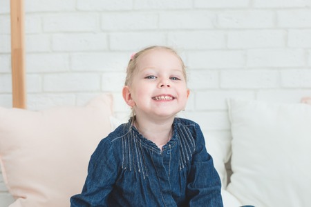 Cute little girl in blue denim overalls sitting on the bed.の写真素材