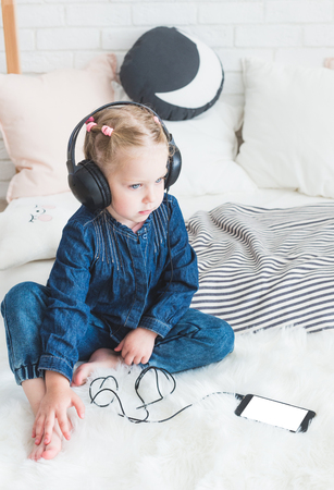 Cute little girl listening to music on headphones at home.の写真素材