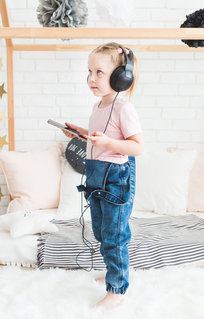 Cute little girl listening to music on headphones at home.の写真素材