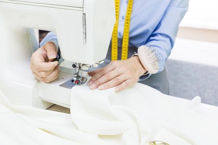 Sewing workshop. Seamstress at work. Young woman working with sewing machine.の写真素材