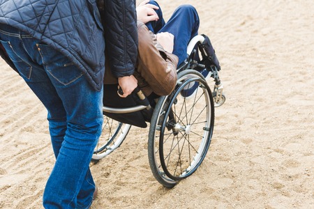Young man in wheelchair with his assistant on a stroll through the park.の写真素材
