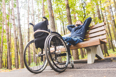 Young man resting sitting on a bench with his legs on his wheelchair.