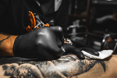 The tattoo artist creates a picture on the body of a man. close-up of tattoo machines and handsの写真素材