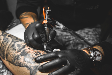 The tattoo artist creates a picture on the body of a man. close-up of tattoo machines and handsの写真素材