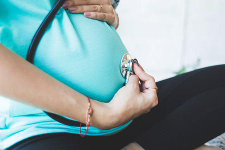 pregnancy, gynecology, medicine, health care and people concept - stethoscope listening to pregnant woman baby heartbeatの写真素材