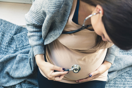 pregnancy, gynecology, medicine, health care and people concept - stethoscope listening to pregnant woman baby heartbeatの写真素材