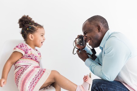 Young father with his cute little daughter taking pictures of each other on an old vintage cameraの写真素材