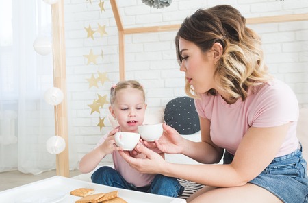 Cute little girl and her mom drink tea with cookies at home.の写真素材