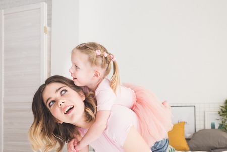Cute little girl and her mom have fun on the bed at home.