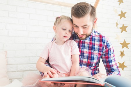 Dad and daughter sit together and read a book.の写真素材