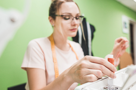 Sewing workshop. Seamstress at work. Young woman working with sewing machine on a colored background
