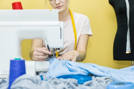 Sewing workshop. Seamstress at work. Young woman working with sewing machine on a colored background