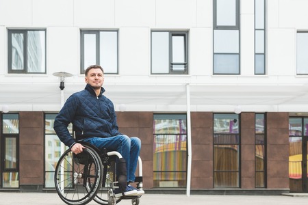 Young man in a wheelchair against the backdrop of a modern high-rise building.