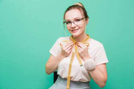 Sewing workshop. Seamstress at work. Portrait of a young dressmaker with measuring tape on a colored background.の写真素材