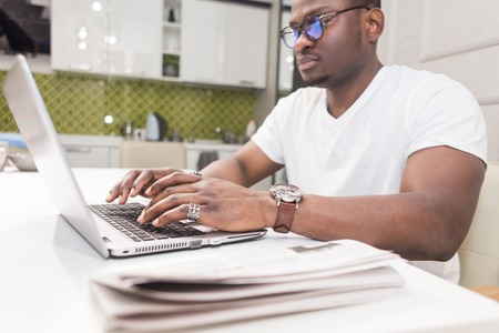 Young African American businessman working on a laptop in the kitchen in a modern interior.の写真素材