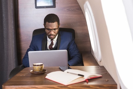 Attractive and successful African American businessman with glasses working on a laptop while...