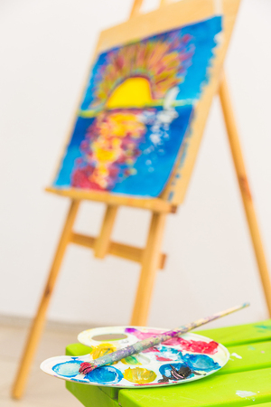 wooden easel in the drawing class with drawings of children. foreground palette. Art class.の写真素材