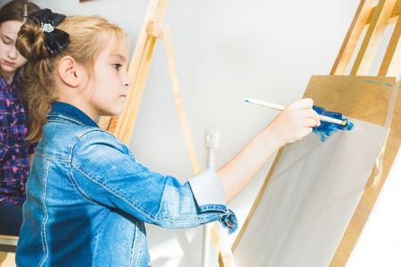 little girl with a teacher in group of preschool student sat the drawing a picture. Painting on maelbert, palette and paints. Back to school and Education concept.の写真素材