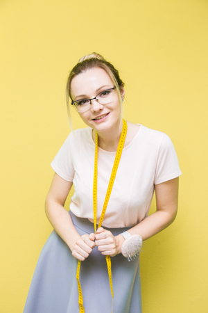 Sewing workshop. Seamstress at work. Portrait of a young dressmaker with measuring tape on a colored background.の写真素材