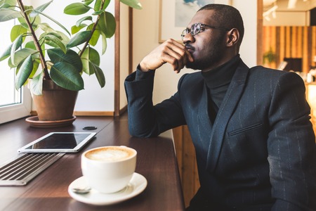 Young handsome dark-skinned businessman drinks coffee in a cafe.の写真素材