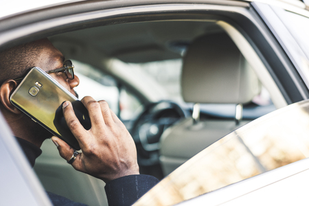 Young successful businessman talking on the phone sitting in the backseat of a expensive car. Negotiations and business meetings.の写真素材