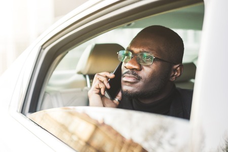 Young successful businessman talking on the phone sitting in the backseat of a expensive car. Negotiations and business meetings.の写真素材