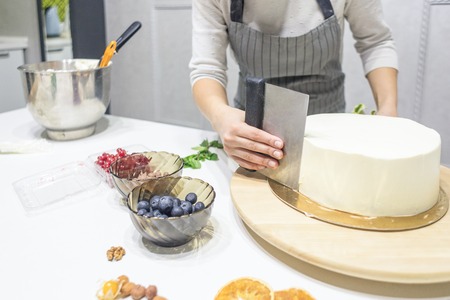 Confectioner smooths white cream on a biscuit cake with a cooking spatula. The concept of homemade pastry, cooking cakes.の写真素材