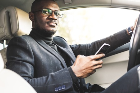 A businessman driving a expensive car holds a mobile phone in his hand. Hasty life.の写真素材