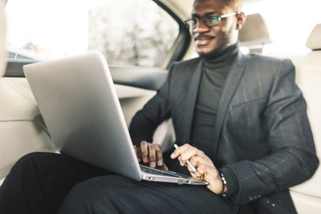Man in a business suit write on laptop in the salon of an expensive car with leather interior.の写真素材
