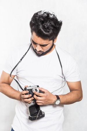 Portrait of a handsome young stylish man with beard taking photo on a vintage camera.の写真素材