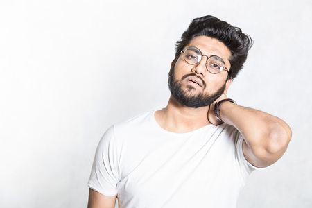 Attractive young man keeps hand on neck, tries to relieve muscle fatigue.