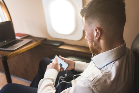 Young attractive and successful businessman is resting and listening to music works while sitting in...